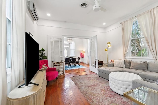 living area featuring wood-type flooring, a wall mounted air conditioner, a ceiling fan, visible vents, and french doors