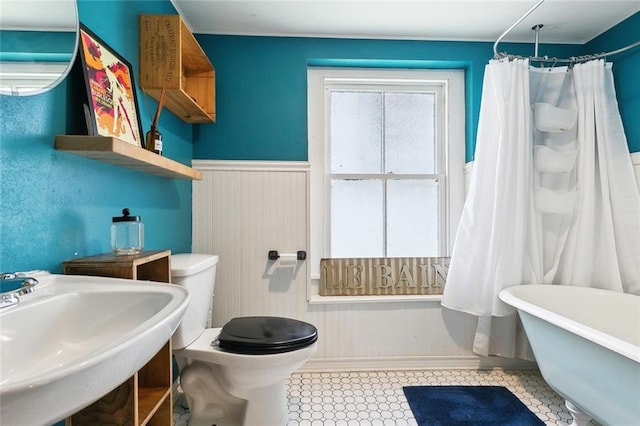 full bathroom with baseboards, a wainscoted wall, toilet, a sink, and a soaking tub