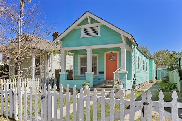 shotgun-style home featuring a gate, a fenced front yard, covered porch, and a chimney