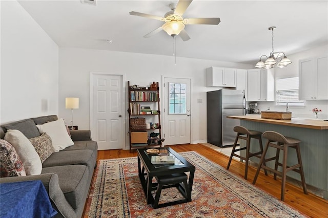 living area featuring visible vents, light wood-style flooring, and ceiling fan with notable chandelier