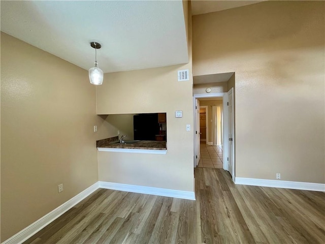 unfurnished living room featuring wood finished floors, visible vents, a sink, and baseboards