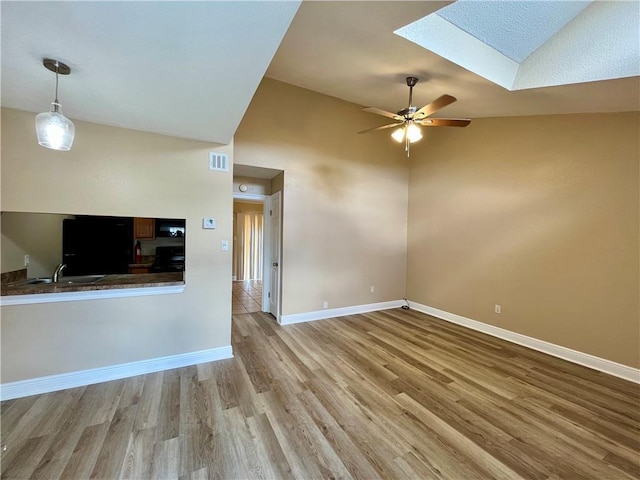 unfurnished living room with lofted ceiling with skylight, wood finished floors, a ceiling fan, and baseboards