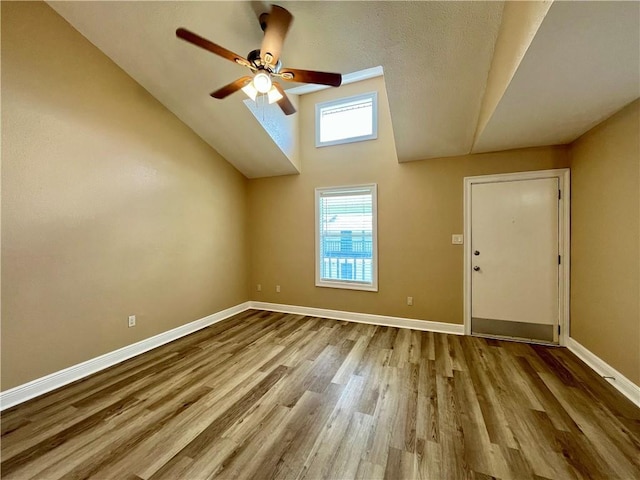 interior space with a ceiling fan, vaulted ceiling, wood finished floors, and baseboards