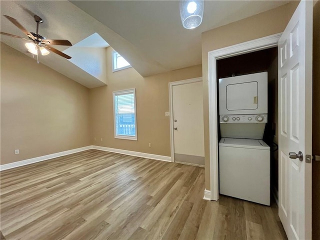 clothes washing area with light wood-style flooring, stacked washer and clothes dryer, ceiling fan, baseboards, and laundry area