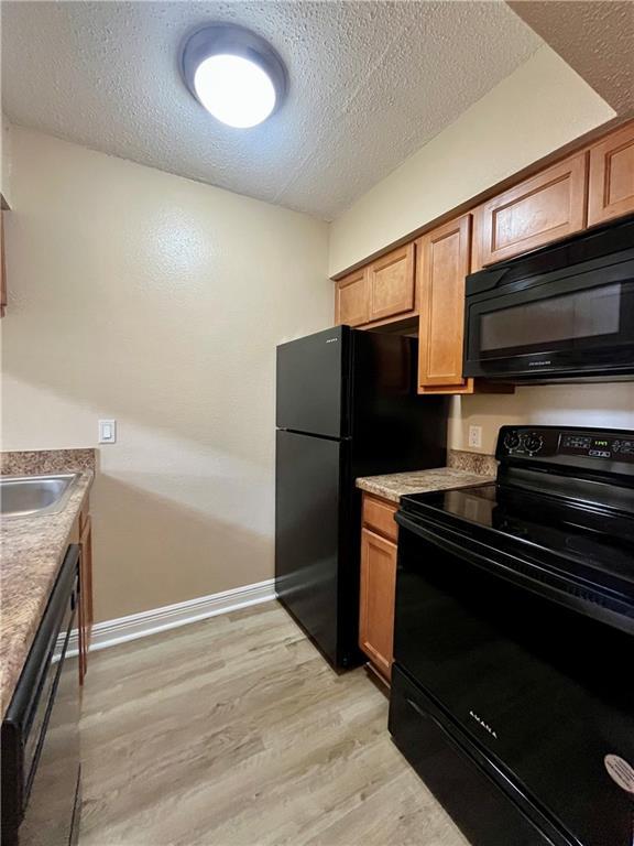 kitchen with black appliances, a textured ceiling, light wood-style flooring, and baseboards
