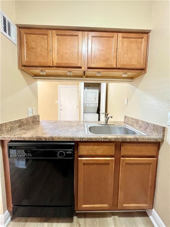 kitchen with a sink, visible vents, light wood-style floors, stacked washing maching and dryer, and black dishwasher