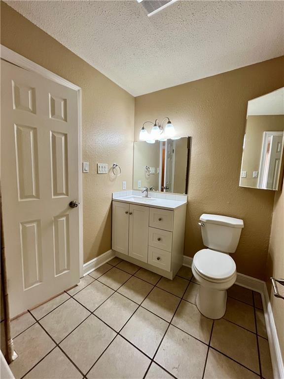bathroom with vanity, toilet, a textured wall, a textured ceiling, and tile patterned flooring