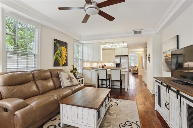 living area featuring dark wood finished floors, visible vents, a ceiling fan, and crown molding