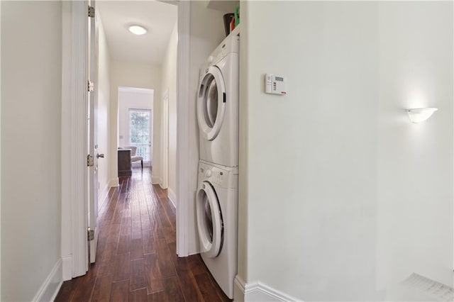 washroom featuring baseboards, stacked washing maching and dryer, laundry area, and dark wood finished floors