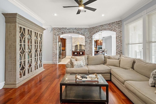 living room featuring ceiling fan, arched walkways, brick wall, wood finished floors, and ornamental molding