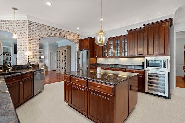kitchen with appliances with stainless steel finishes, hanging light fixtures, a sink, beverage cooler, and arched walkways