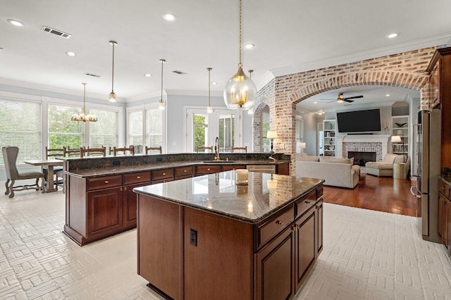 kitchen featuring crown molding, a fireplace, ceiling fan with notable chandelier, a center island, and visible vents