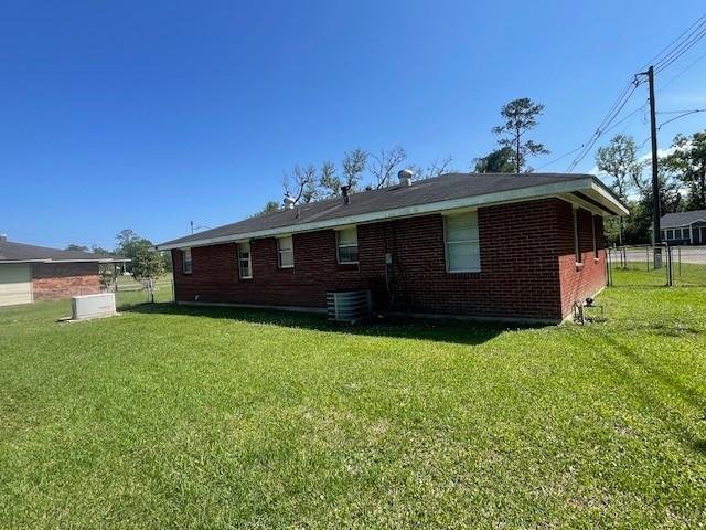 rear view of property with a yard, central air condition unit, and brick siding