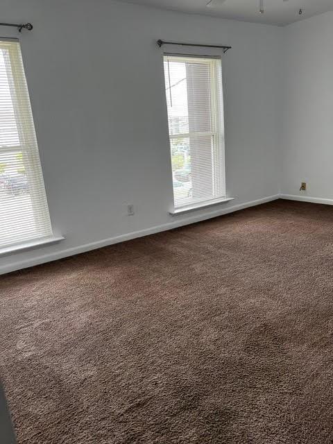 unfurnished room featuring dark colored carpet and baseboards