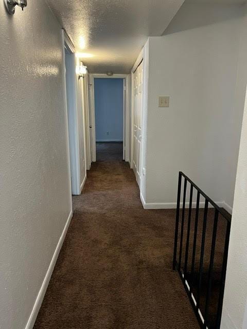 corridor with a textured wall, carpet, and baseboards
