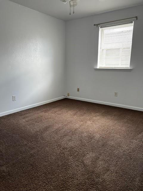 unfurnished room with dark colored carpet and baseboards