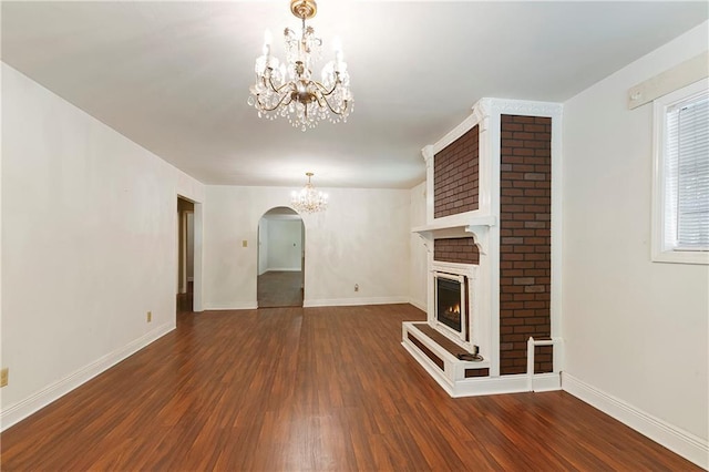 2751 Washington Ave, Slidell, LA 70458 - unfurnished living room with a chandelier, dark wood-style flooring, a lit fireplace, baseboards, and arched walkways