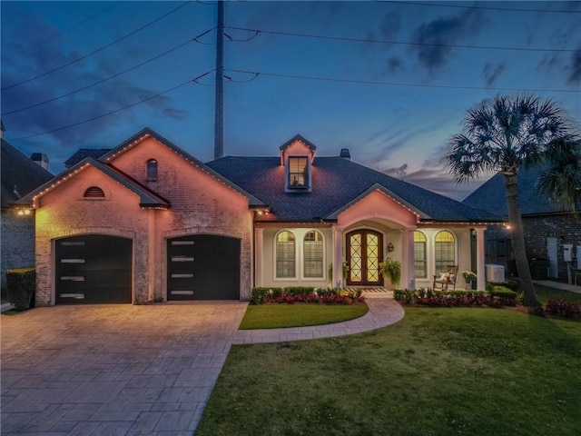 mediterranean / spanish-style home featuring a front lawn, decorative driveway, brick siding, an attached garage, and french doors