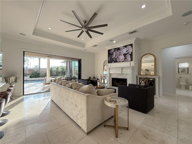 living room with a raised ceiling, a ceiling fan, visible vents, ornamental molding, and a high end fireplace