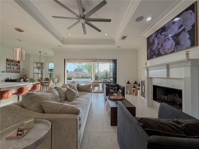 living room with visible vents, ceiling fan, a tray ceiling, a high end fireplace, and ornamental molding