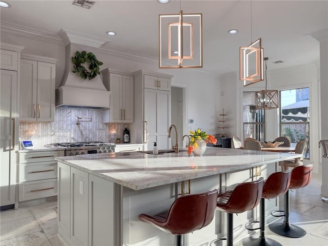 kitchen with light stone countertops, a sink, a large island, tasteful backsplash, and custom exhaust hood