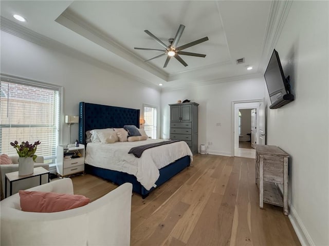 bedroom featuring light wood-type flooring, a tray ceiling, visible vents, baseboards, and ornamental molding