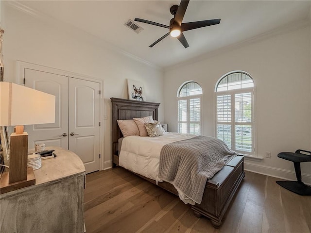 bedroom with crown molding, visible vents, a closet, baseboards, and dark wood finished floors