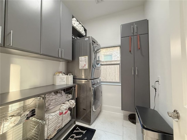 laundry area featuring light tile patterned flooring, cabinet space, stacked washer and clothes dryer, and baseboards