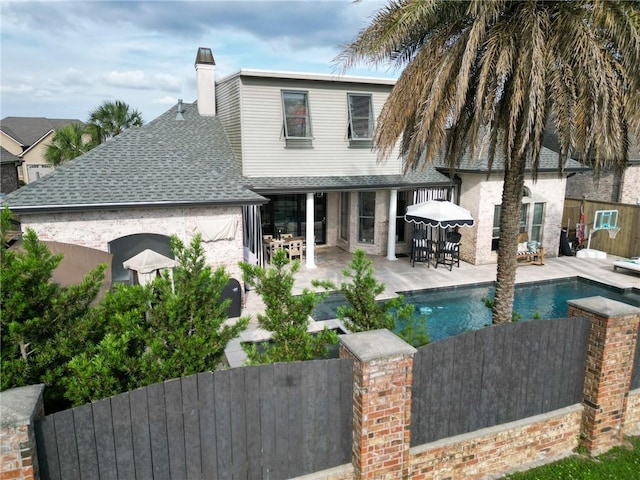 rear view of property featuring a shingled roof, a patio area, a fenced in pool, fence private yard, and a chimney
