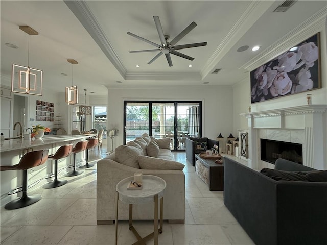 living area featuring visible vents, a tray ceiling, a high end fireplace, ornamental molding, and a ceiling fan