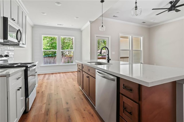kitchen featuring a sink, appliances with stainless steel finishes, light wood-type flooring, light stone countertops, and decorative light fixtures
