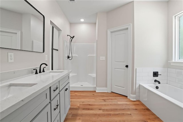 full bath with a sink, a bath, double vanity, walk in shower, and wood finished floors