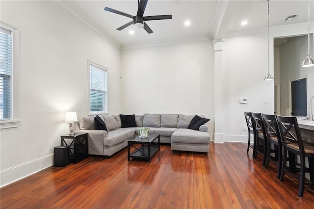 living area with dark wood-type flooring, crown molding, a ceiling fan, visible vents, and baseboards