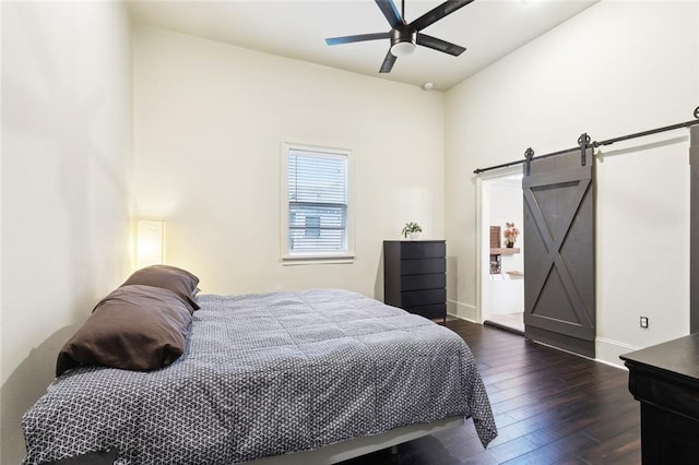 bedroom featuring a ceiling fan, baseboards, a barn door, and dark wood finished floors