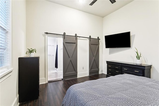 bedroom with baseboards, a barn door, ceiling fan, and dark wood-style flooring