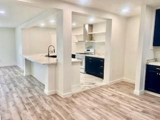 kitchen with light wood-type flooring, light countertops, white electric range oven, and wall chimney range hood