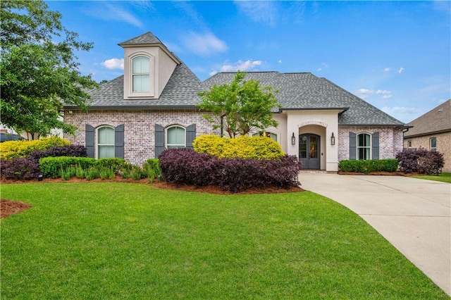 french provincial home featuring a front lawn, a shingled roof, and brick siding