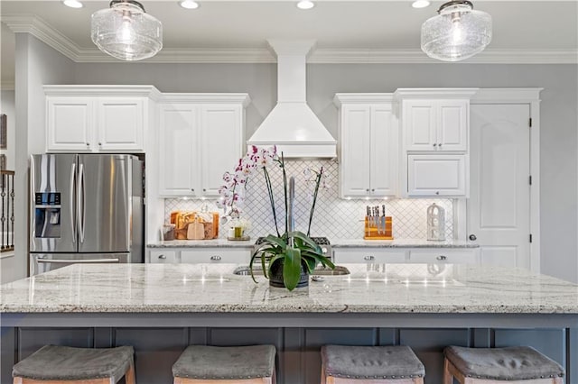 kitchen featuring a kitchen island with sink, white cabinets, stainless steel refrigerator with ice dispenser, and a breakfast bar