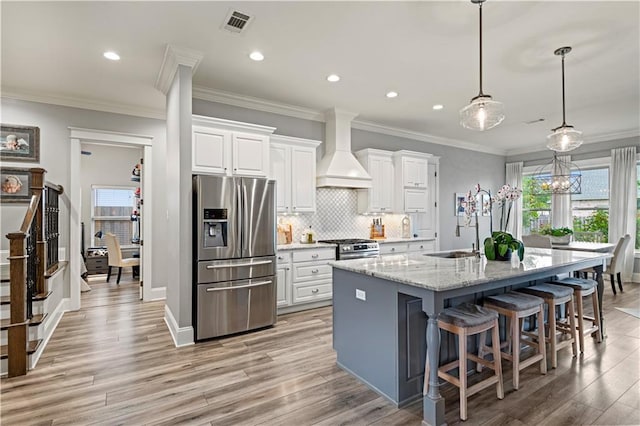 kitchen featuring white cabinetry, a sink, appliances with stainless steel finishes, custom exhaust hood, and an island with sink