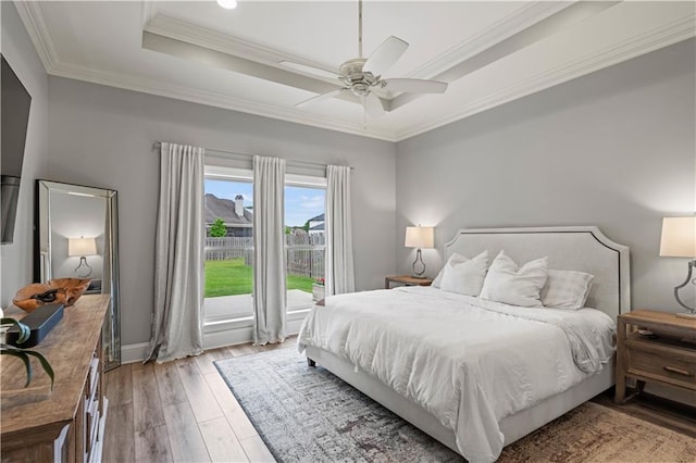 bedroom featuring a raised ceiling, a ceiling fan, ornamental molding, and light wood-style floors