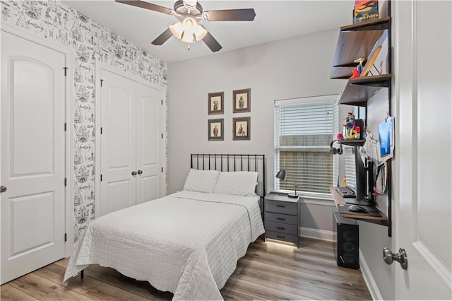 bedroom featuring wood finished floors, wallpapered walls, a closet, baseboards, and a ceiling fan