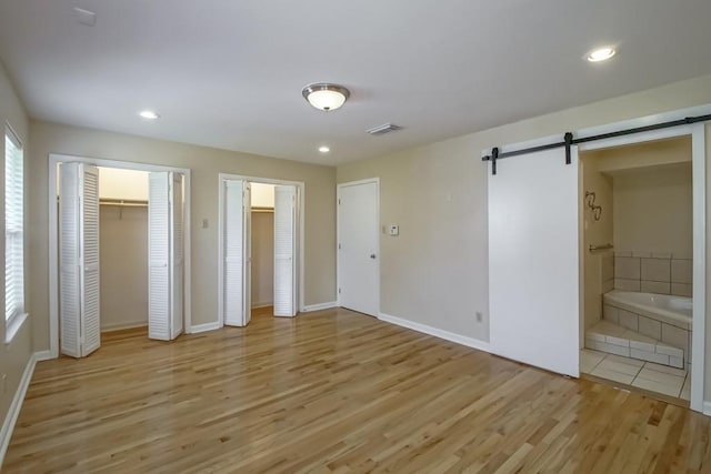 5 N Lafourche Ct, Kenner, LA 70065 - unfurnished bedroom featuring visible vents, a barn door, baseboards, light wood finished floors, and multiple closets