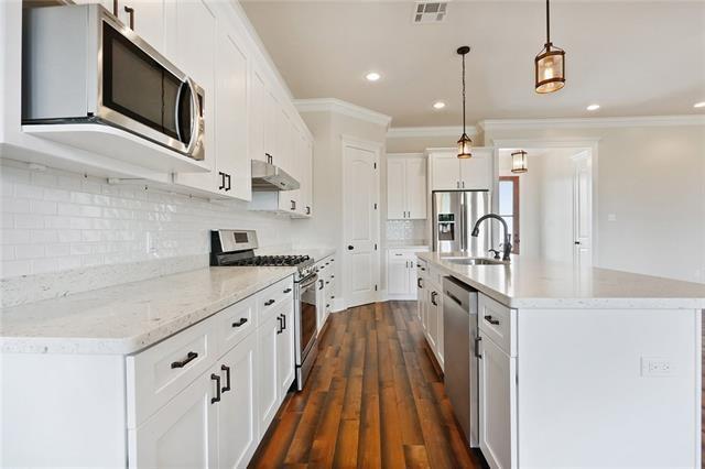 kitchen featuring a sink, stainless steel appliances, under cabinet range hood, visible vents, and ornamental molding