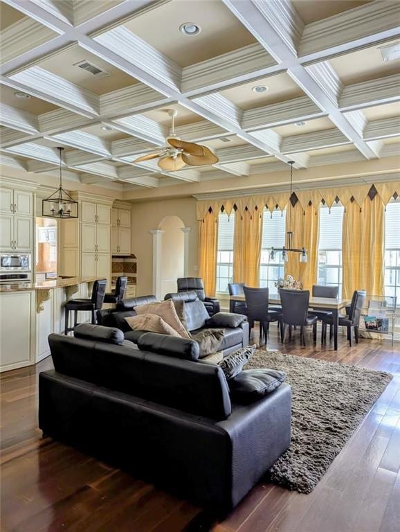 living room featuring coffered ceiling, arched walkways, beam ceiling, and ceiling fan with notable chandelier