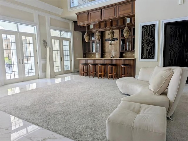 living area with a high ceiling, marble finish floor, french doors, and indoor bar