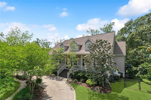 cape cod house with a front lawn, fence, covered porch, stairs, and a shingled roof