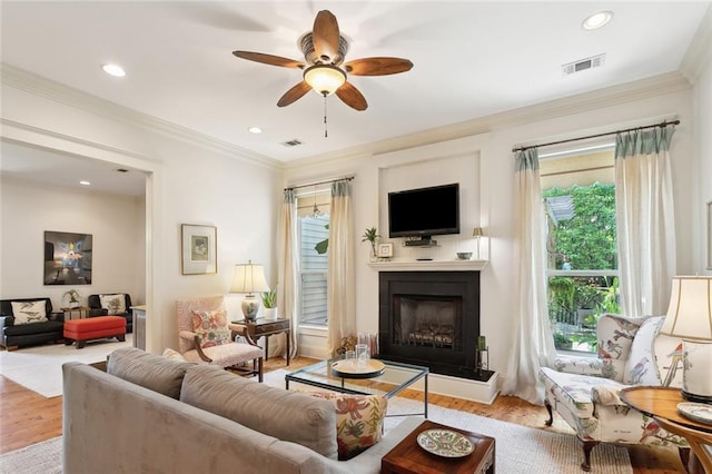 living area featuring visible vents, a fireplace with raised hearth, a ceiling fan, and wood finished floors
