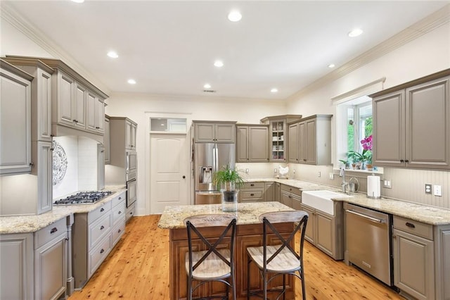kitchen with a kitchen island, appliances with stainless steel finishes, gray cabinetry, a sink, and a breakfast bar