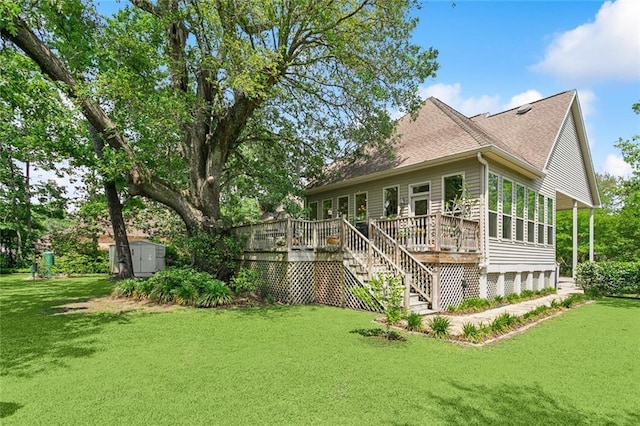 rear view of property featuring a wooden deck, a yard, a shingled roof, a storage shed, and an outbuilding