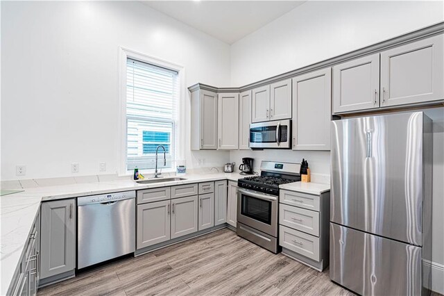 1379 Saint Anthony St, New Orleans, LA 70116 - kitchen featuring light stone counters, a sink, stainless steel appliances, light wood-type flooring, and gray cabinetry